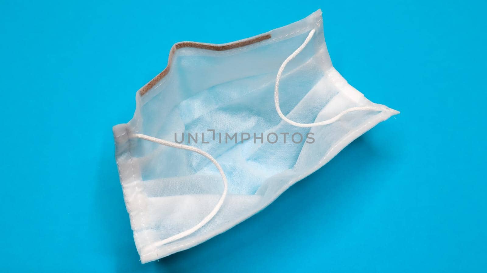One 3-ply disposable surgical face mask with rubber grips covering mouth and nose against blue background. Protection from bacteria, healthcare and medicine concept. COVID-19. A dangerous virus