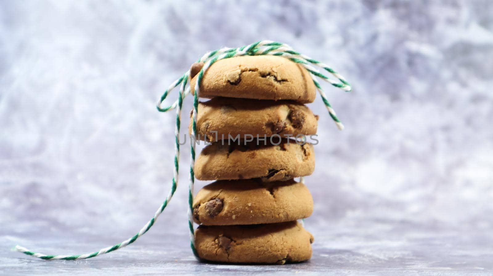 American chocolate chip cookies stacked on top of each other with green thread on a gray background. Traditional rounded crunchy dough with chocolate chips. Bakery. Delicious dessert, pastries