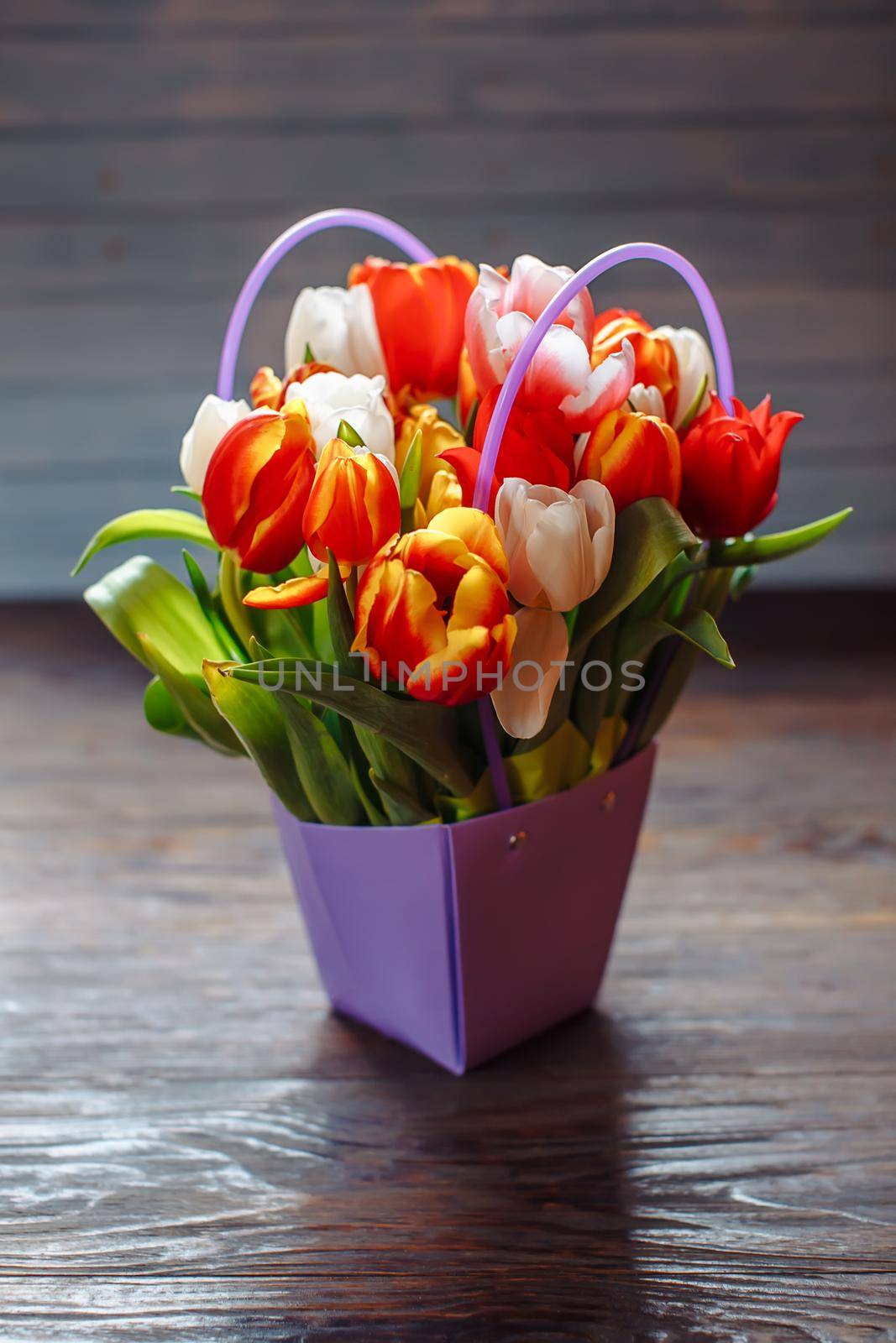 bouquet of different color tulips in purple box on a dark wooden background at springtime