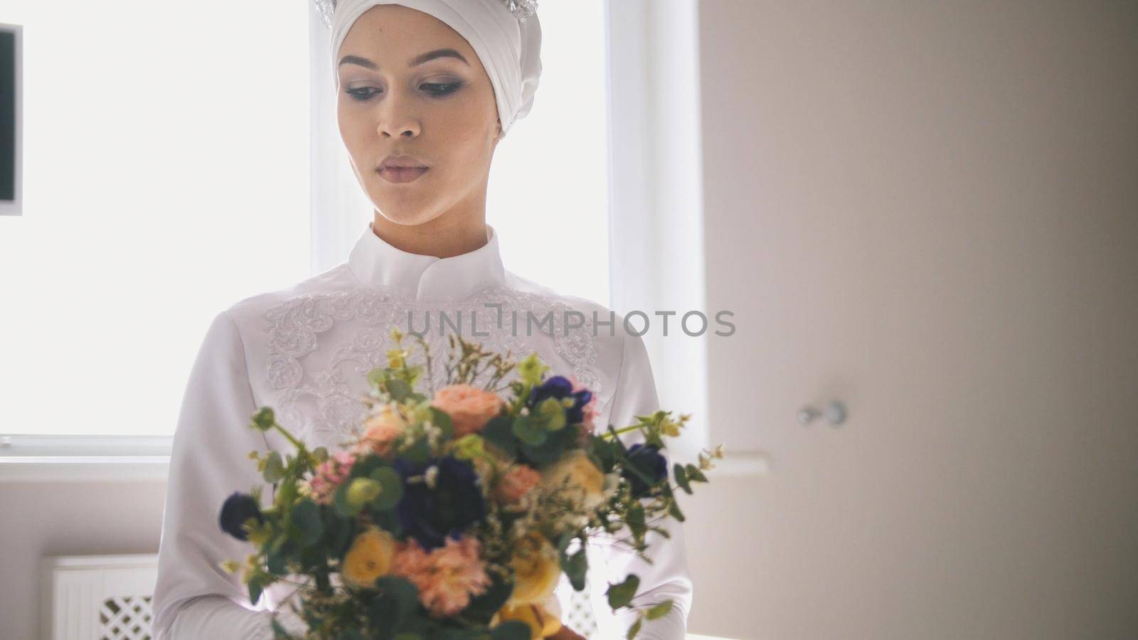 Portrait of young woman in traditional islamic wedding dress holding the bouquet of flowers, close up