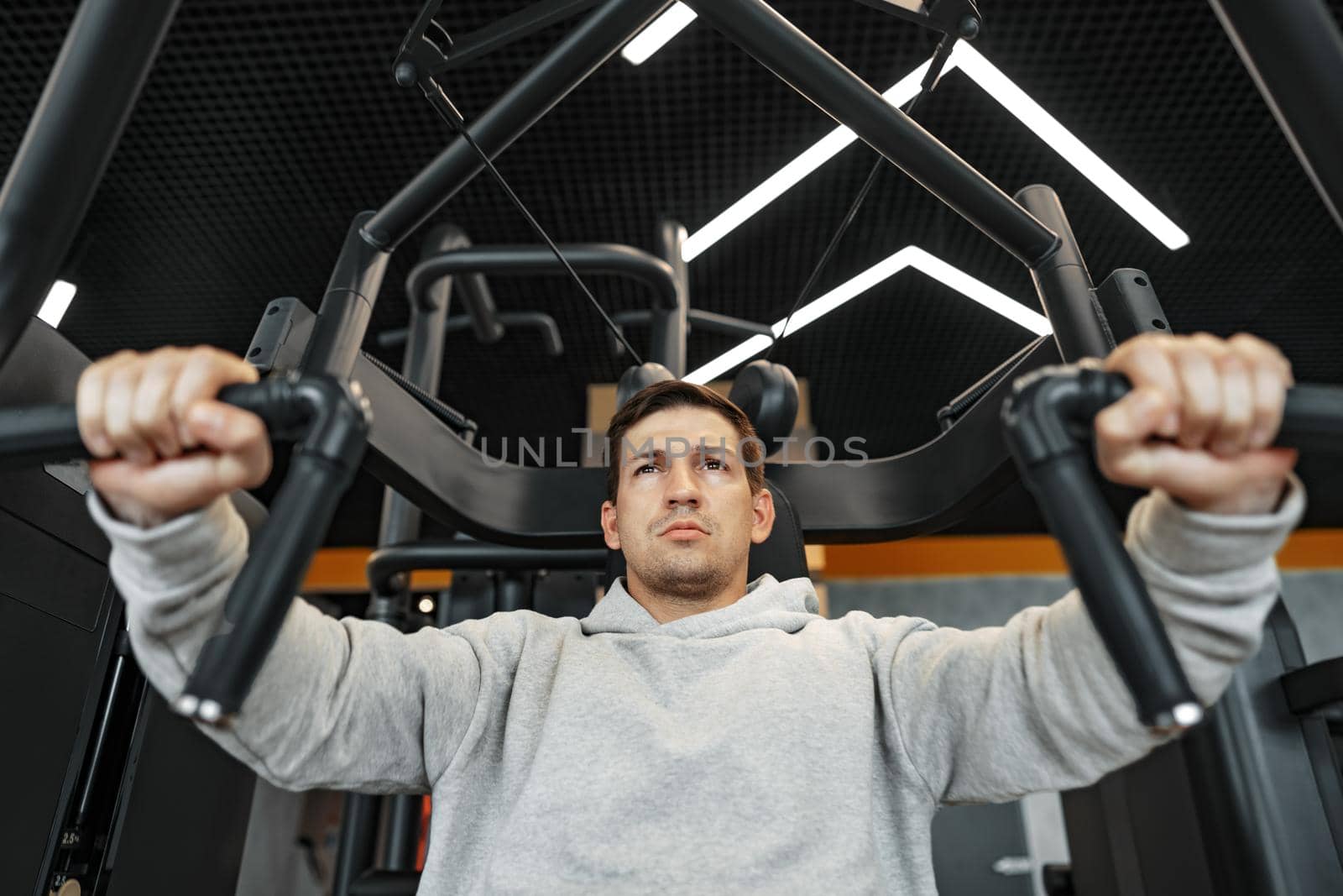 Young fit bodybuilder man doing arms workout training in the gym on machine, close up