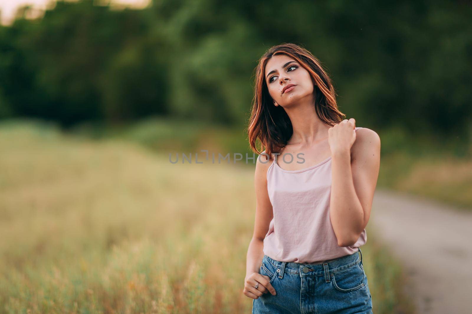 Portrait of beautiful sexy young woman with long brown hair in pink tank top and denim shorts posing outdoors, sensual, serious by OnPhotoUa