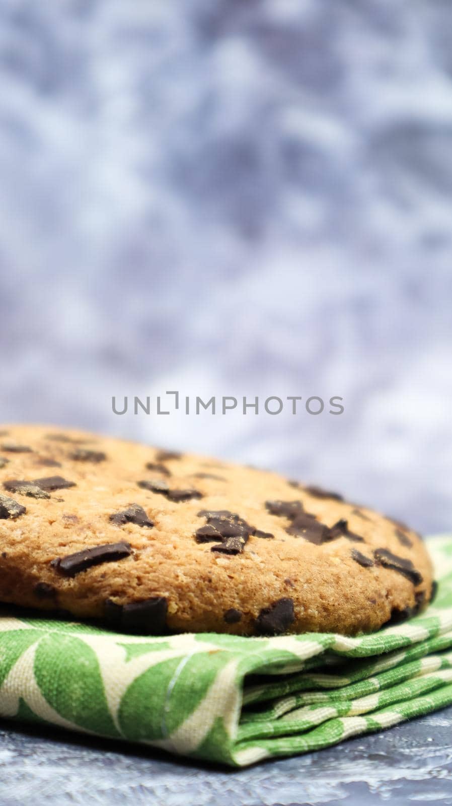 American chocolate chip cookies on a green napkin on a gray background. Traditional round crispy dough with chocolate chips. Bakery. Delicious dessert, pastries. Vertical photography.