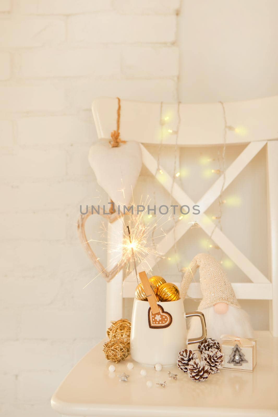 White cup with golden balls and sparklers. Cute gnome with long beard. white cristmas hearts, pine cones and warm lights on brick wall