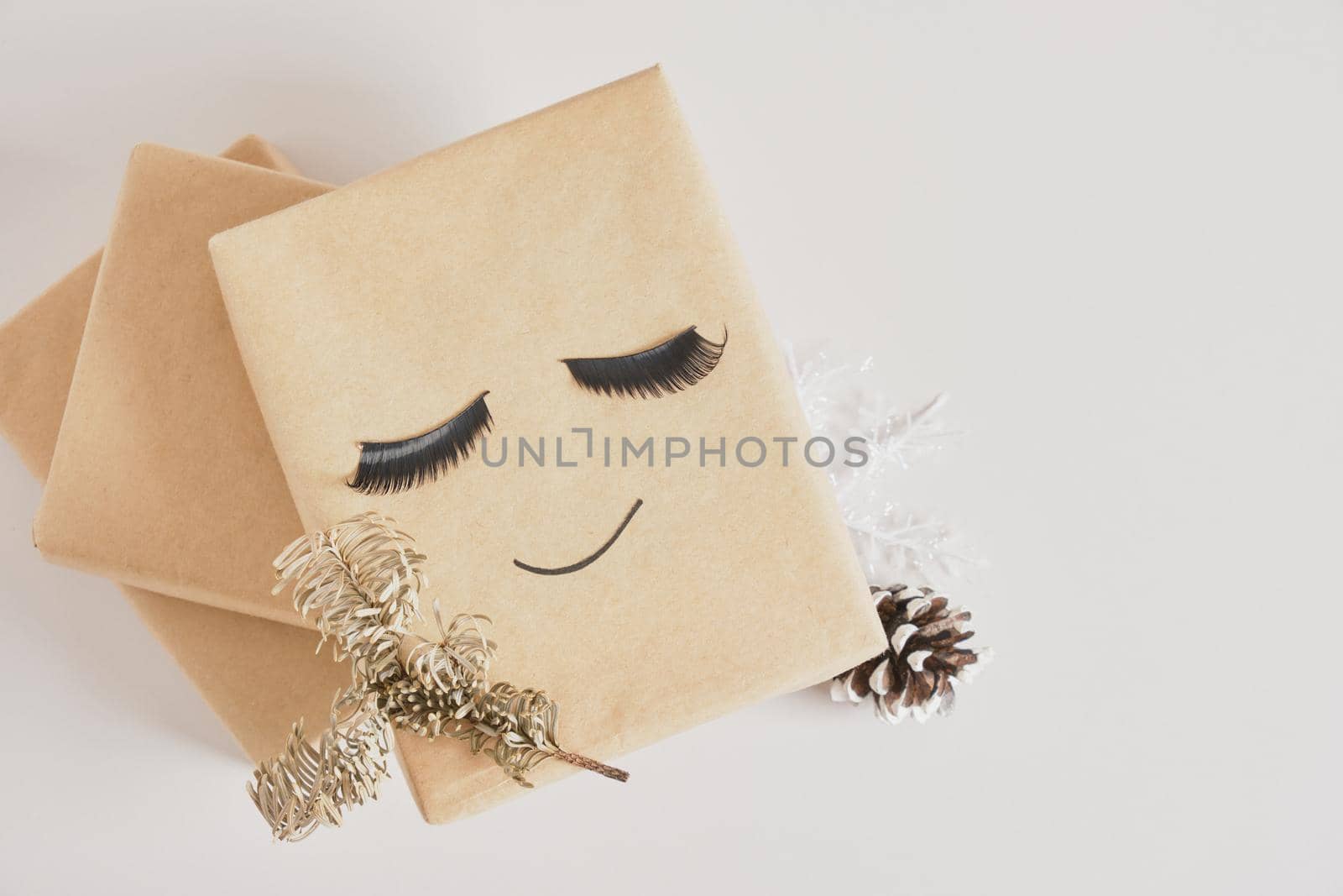 gift boxes with kraft paper on gray background, original gift decor with false eyelashes and minimalistic eco-friendly christmas decor, spruce branch and pine cone