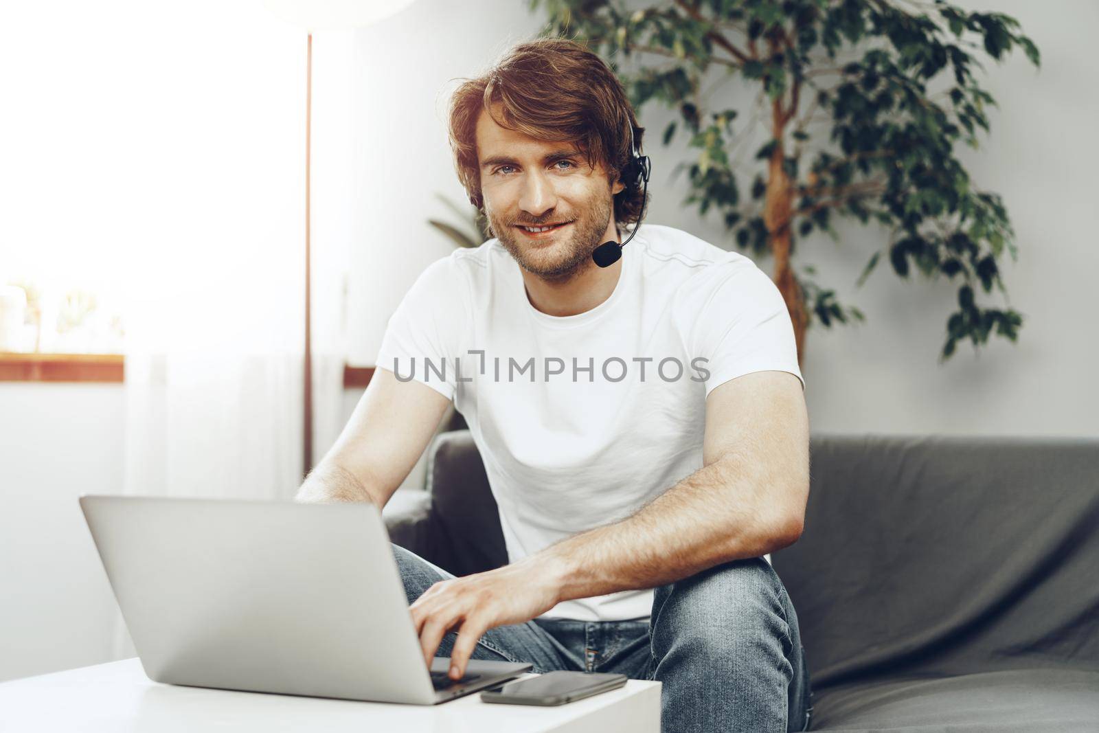 Young man businessman with headset working on laptop from home. Home office concept