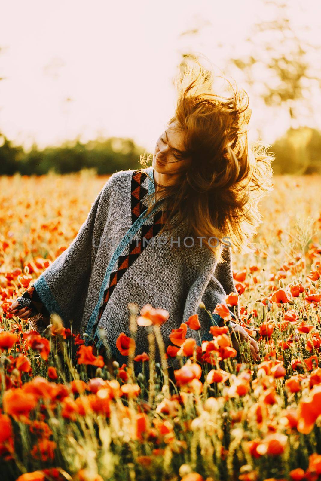 Freedom happy beautiful young woman relaxing in poppy flower field on sunny summer day, her hair fly-away.