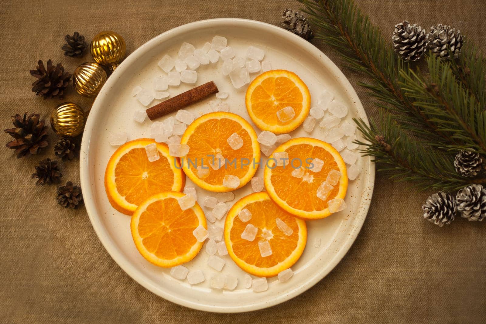 oranges at the plate near christmas tree branch, candies, cinnamon, golden balls and pine cones. Cristmas decorations. Tangerines and on plate