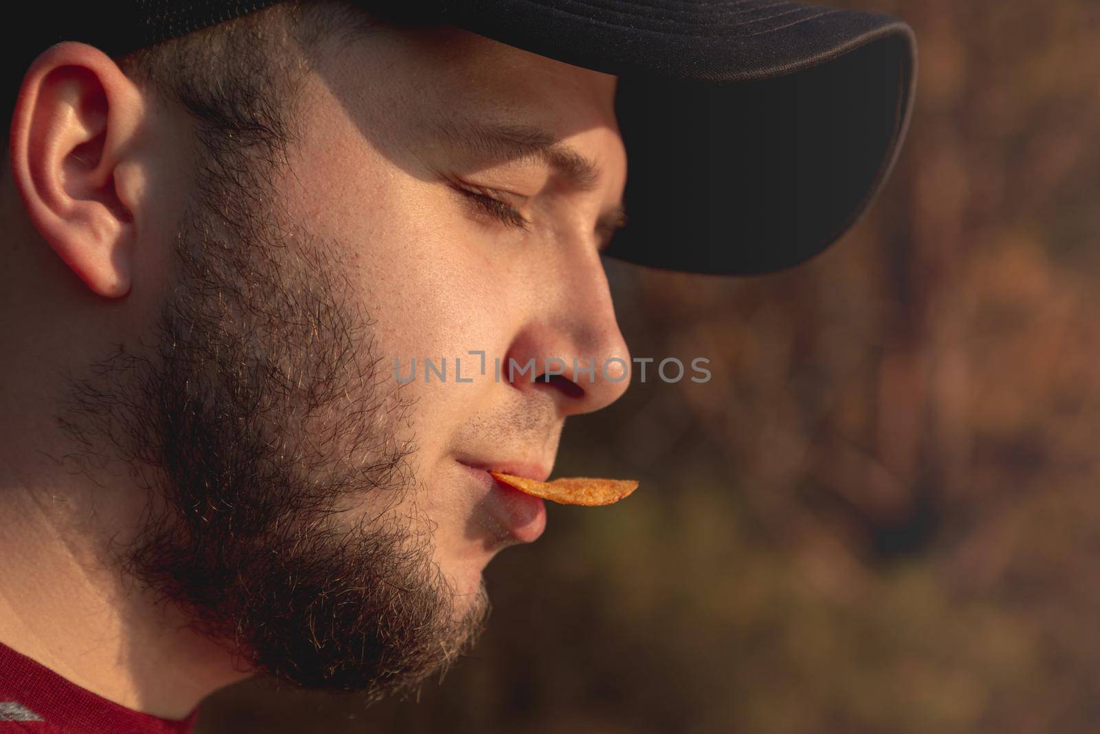 Bearder Man in forest eating chips. In park image outdoors with blurred background.