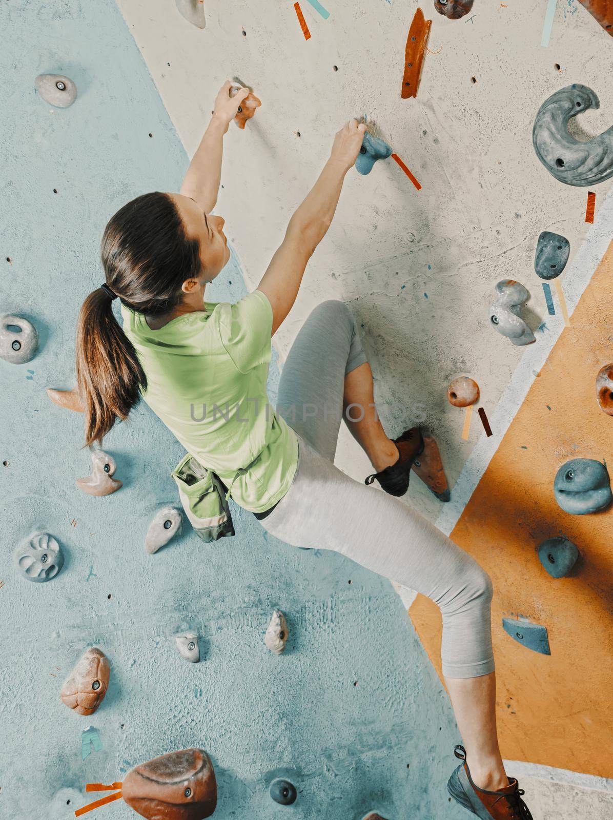 Sporty young woman free climbing on practical wall in gym, bouldering.