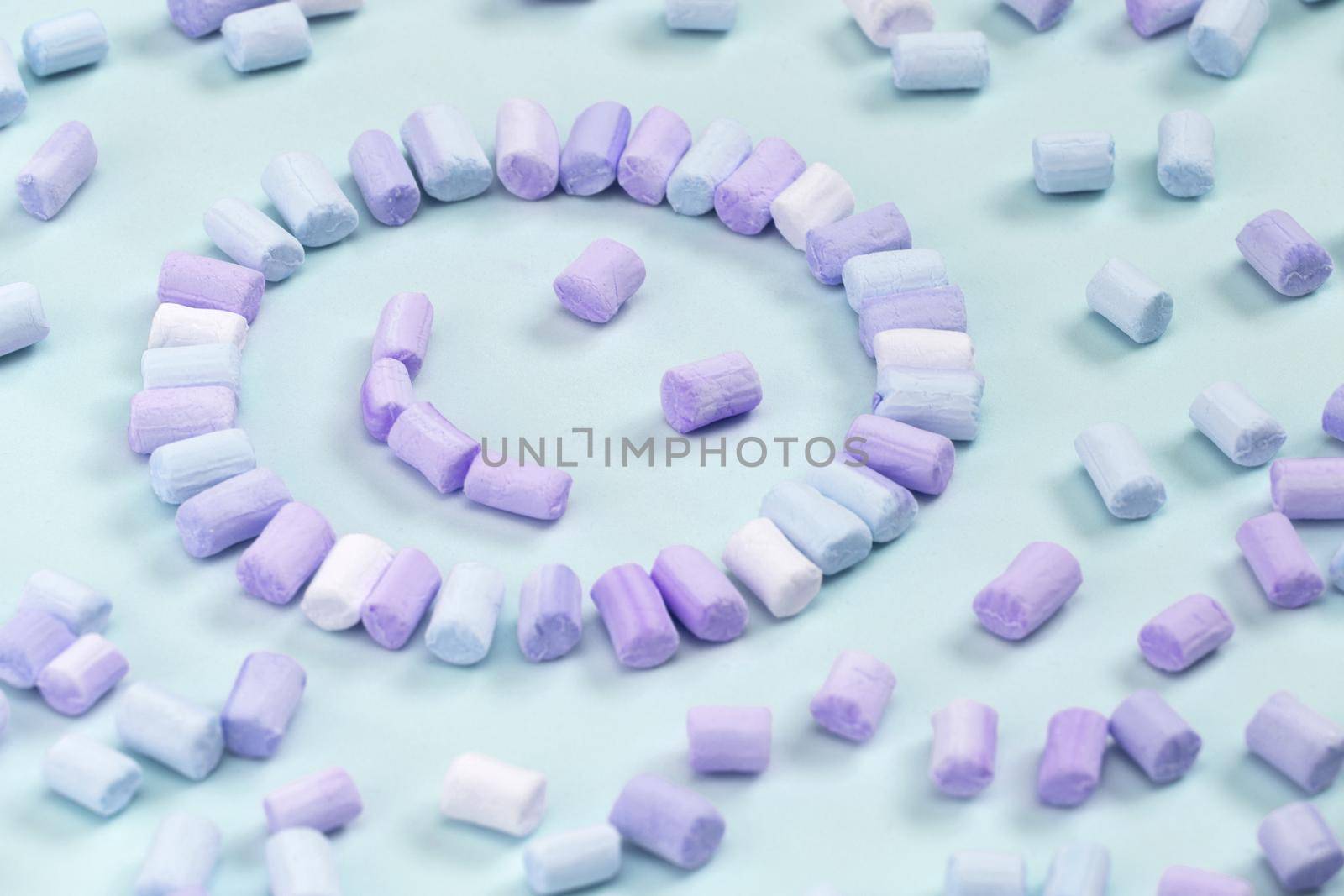 Top view of the multi-colored marshmallows which lies in the shape of a smiley or sun on a one-color pink background.