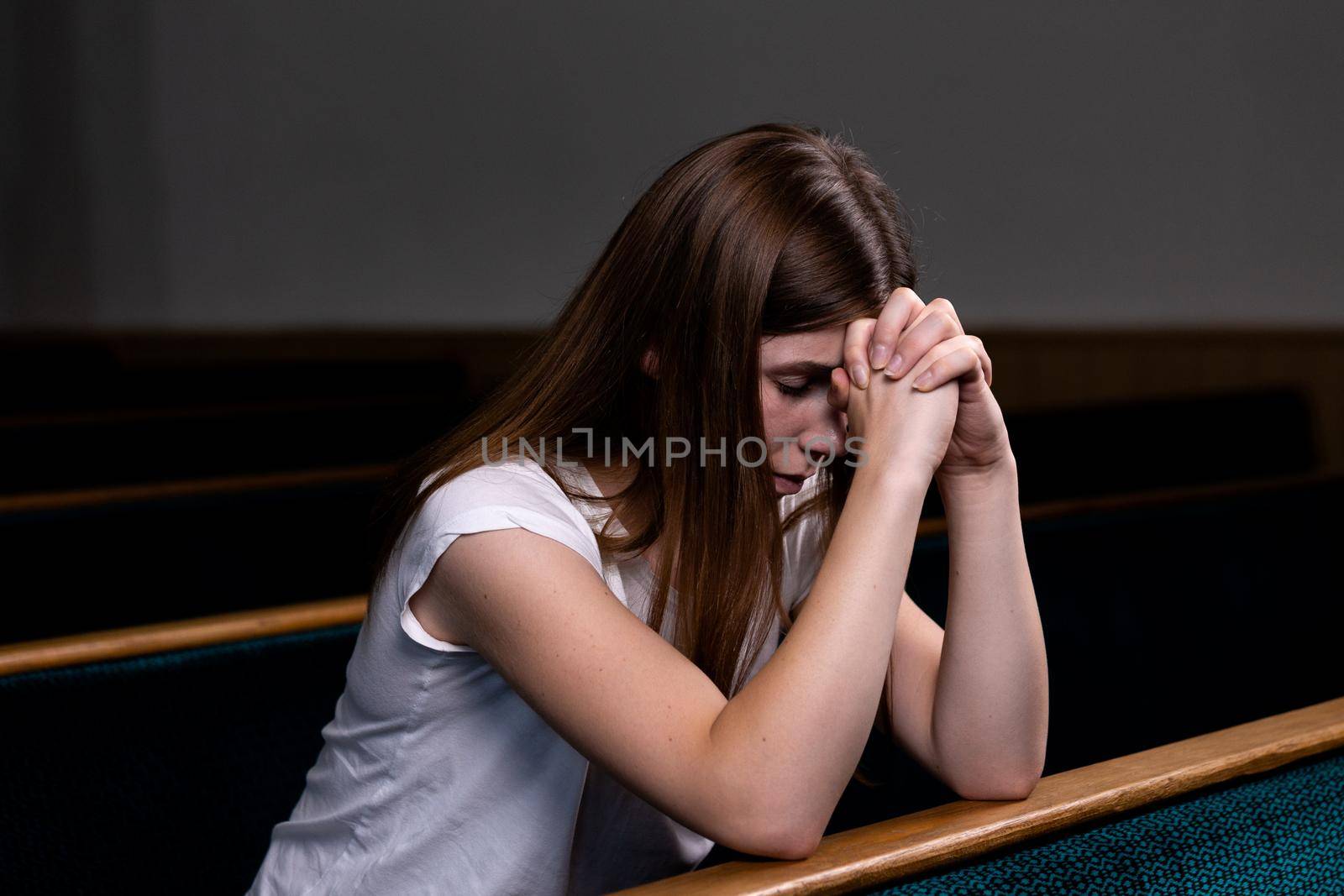 A Sad Christian girl in white shirt is sitting and praying with humble heart in the church by lunarts