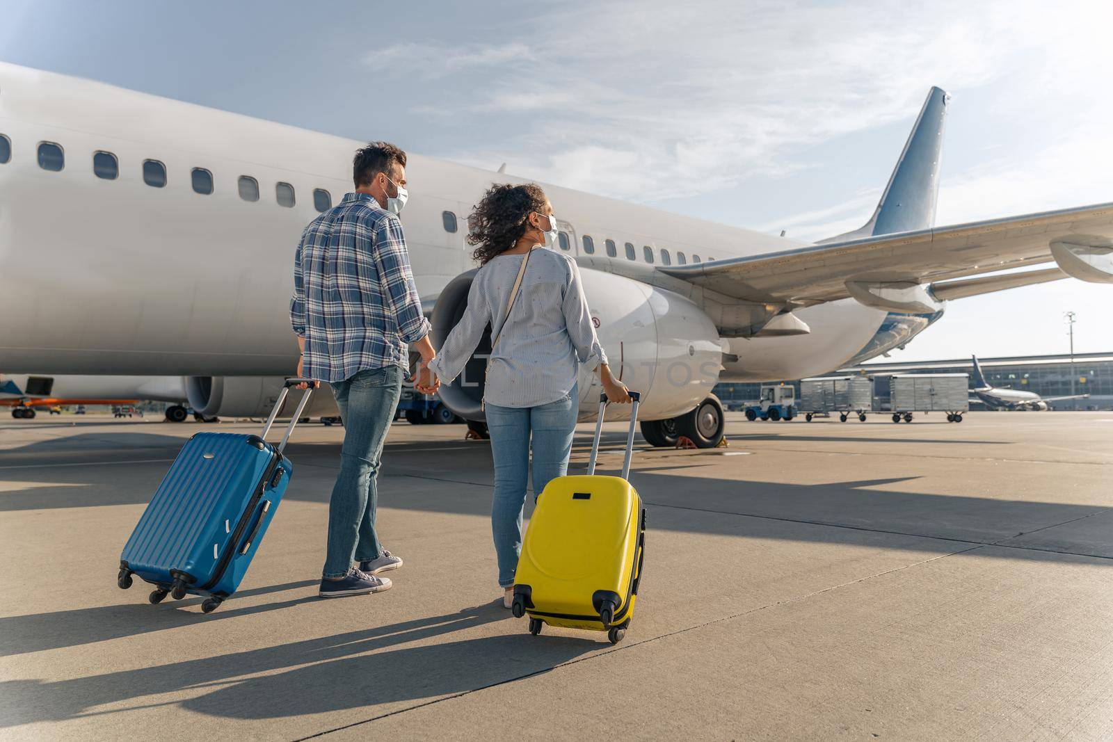 Back view of man and woman wearing protective masks and walking with suitcases. Trip concept