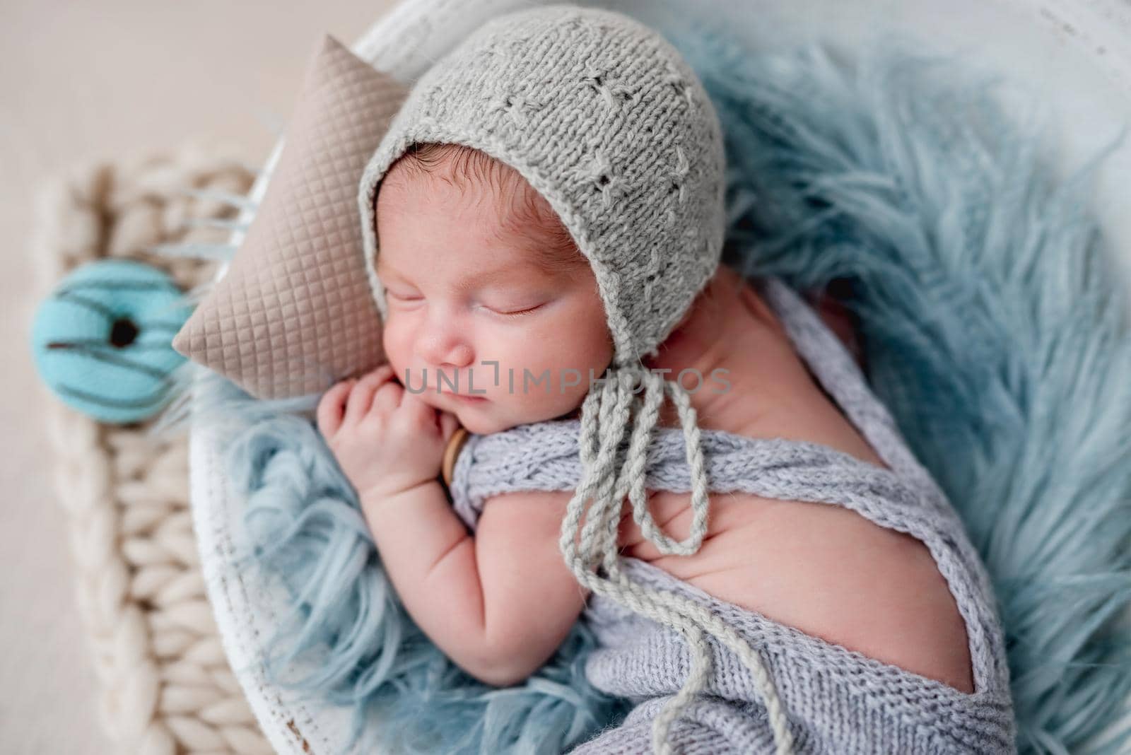 Cute newborn sleeping in round cradle beside knitted donut