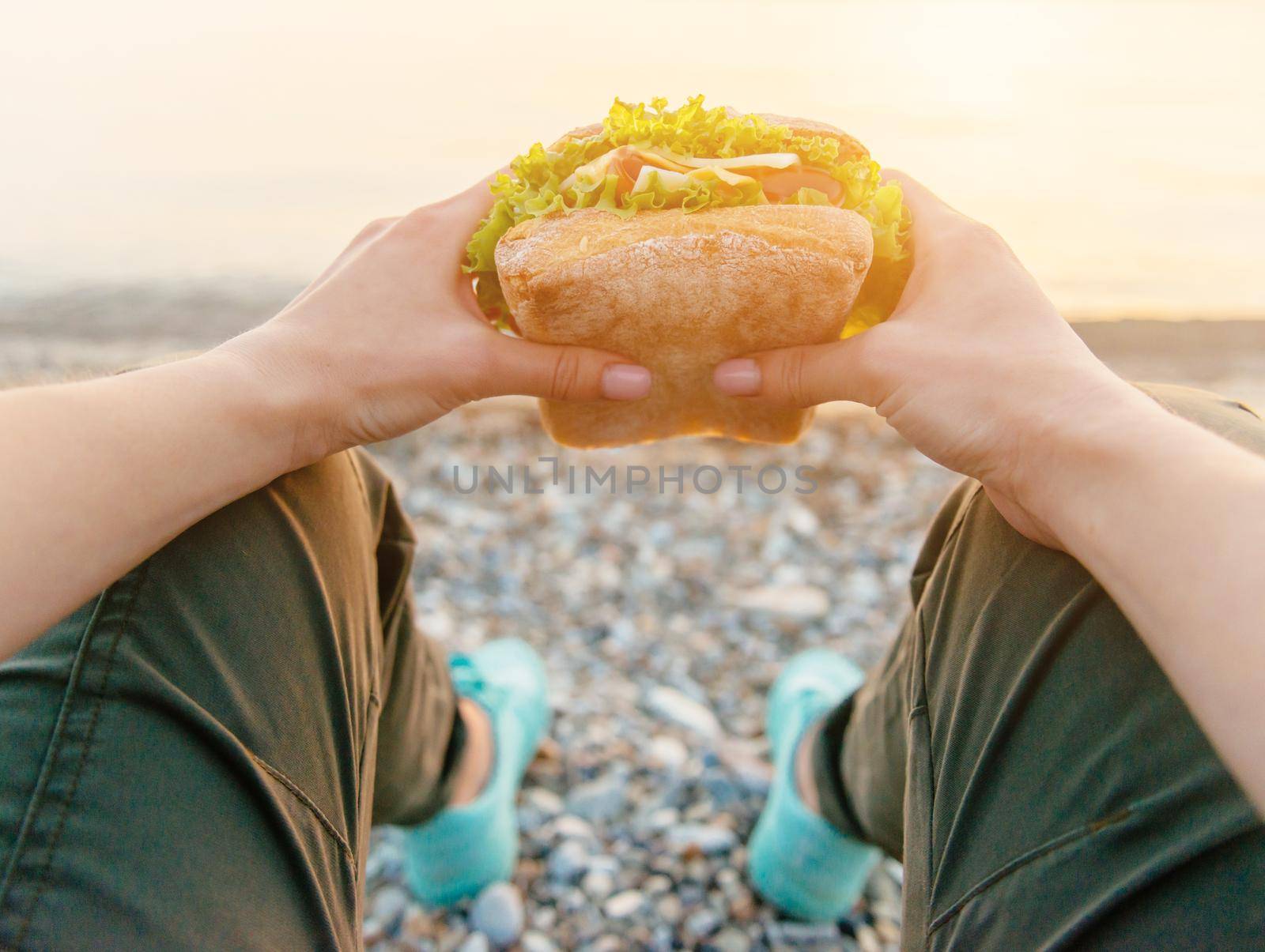 Young woman holding and ready to eat fresh fast food burger sandwich while resting on nature outdoor, point of view.