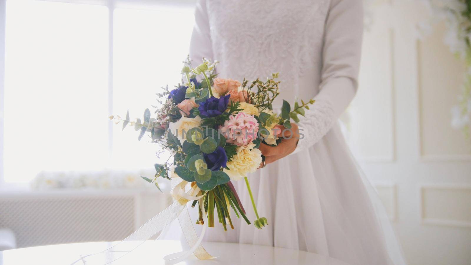 Hands of muslim bride in white dress holding the bouquet of flowers, horizontal