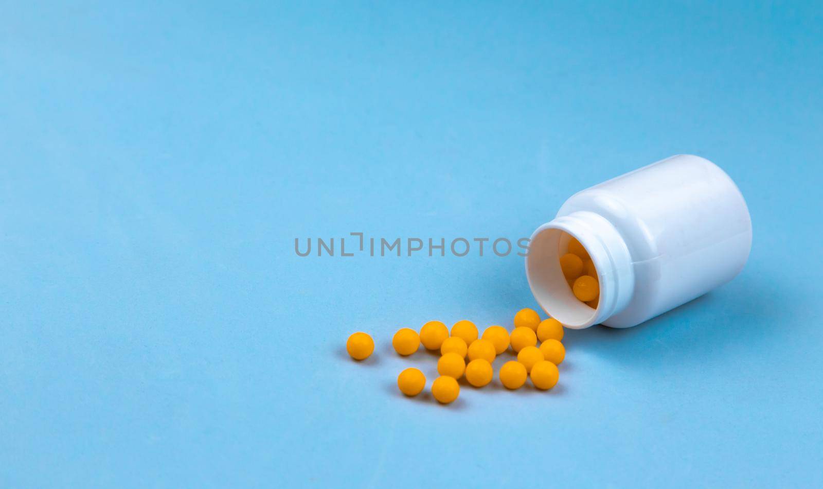 Yellow pills and plastic white bottle. Blue background with copy space for text