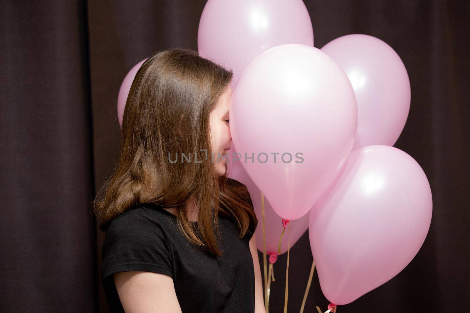 A cute young girl faces her pink balls, which she holds and smiles on a dark background.