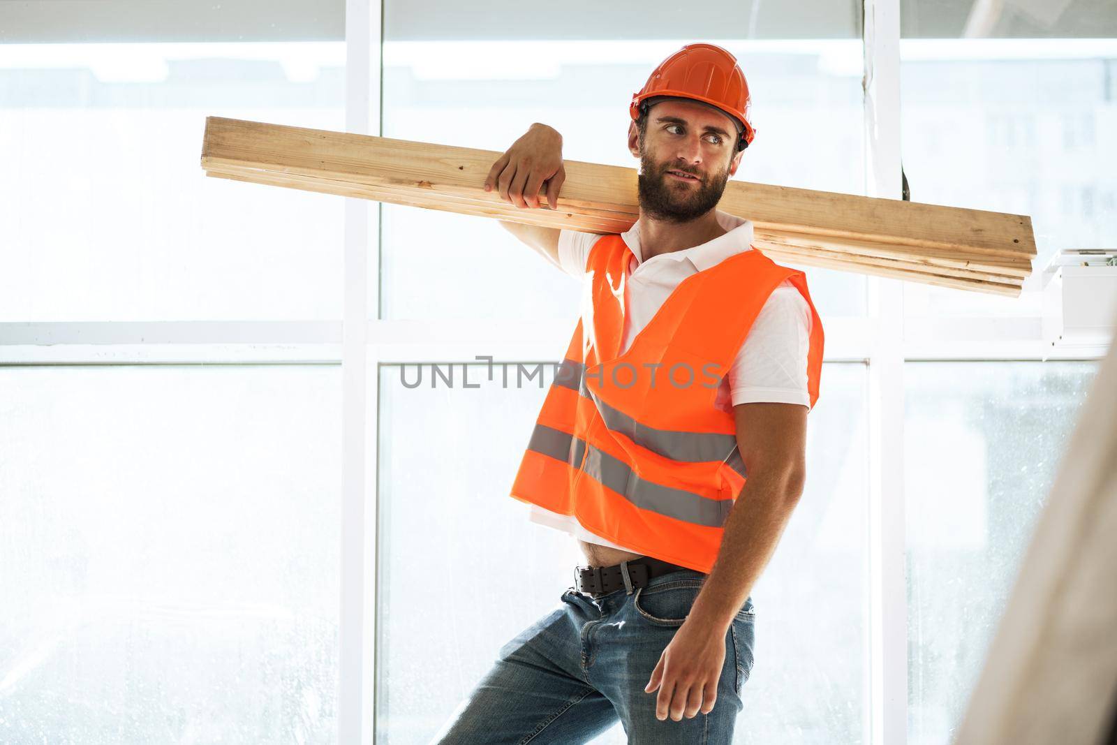 Builder man in hardhat carrying timber on building site, close up portrait