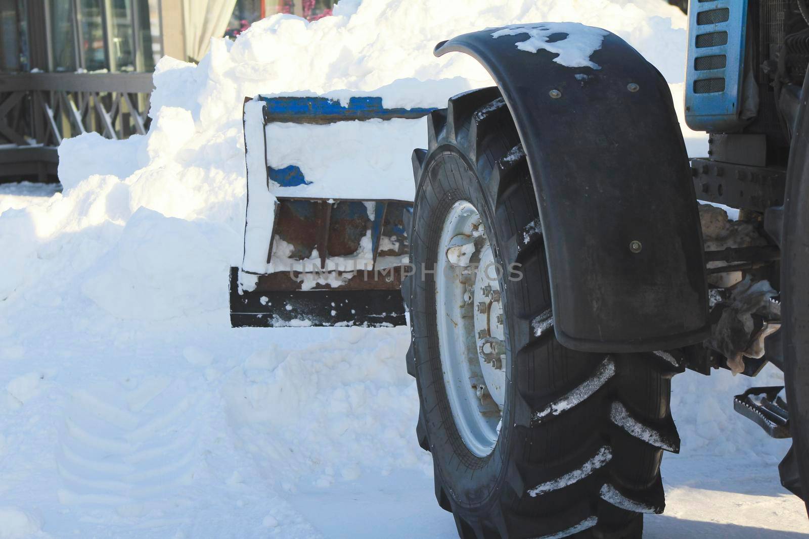 Clearing snow from the road with bulldozer in the city in winter, focus on blade and wheel, urban landscape