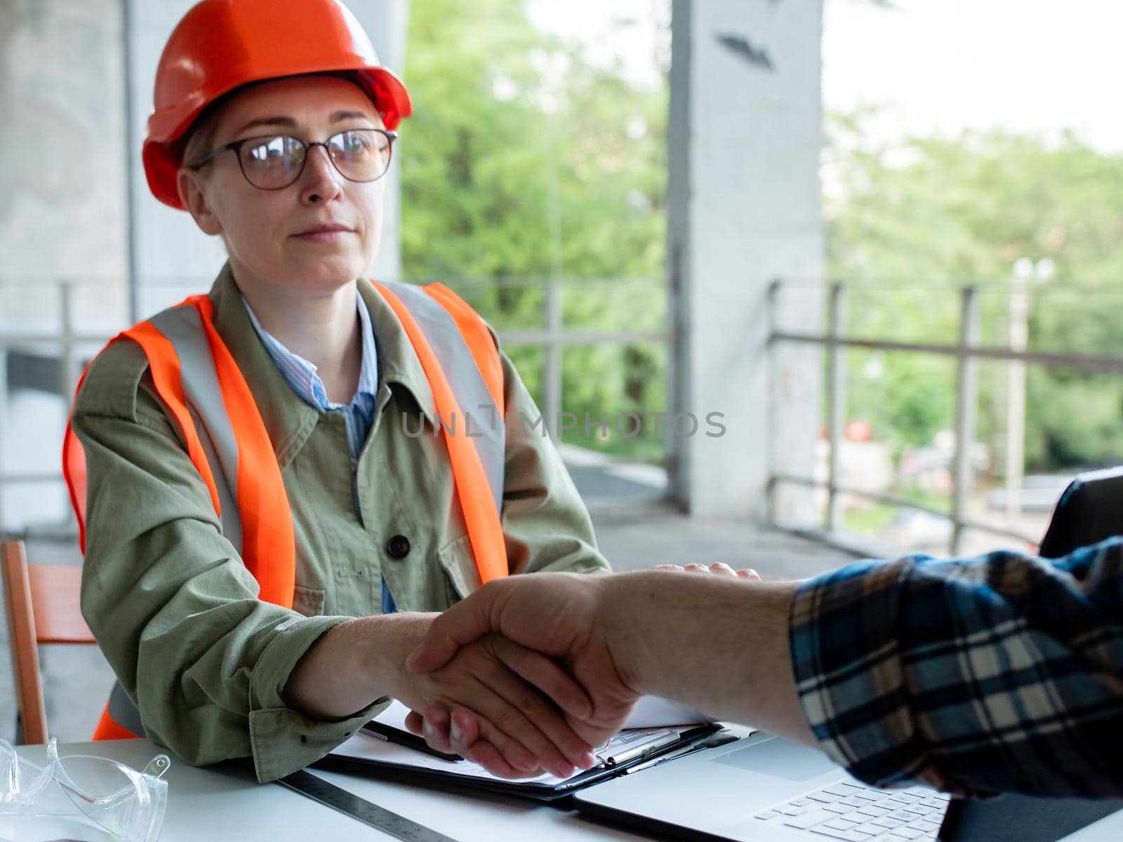 A male engineer and a female construction engineer in a safety helmet shake hands and are ready to work together on a construction project. by Utlanov