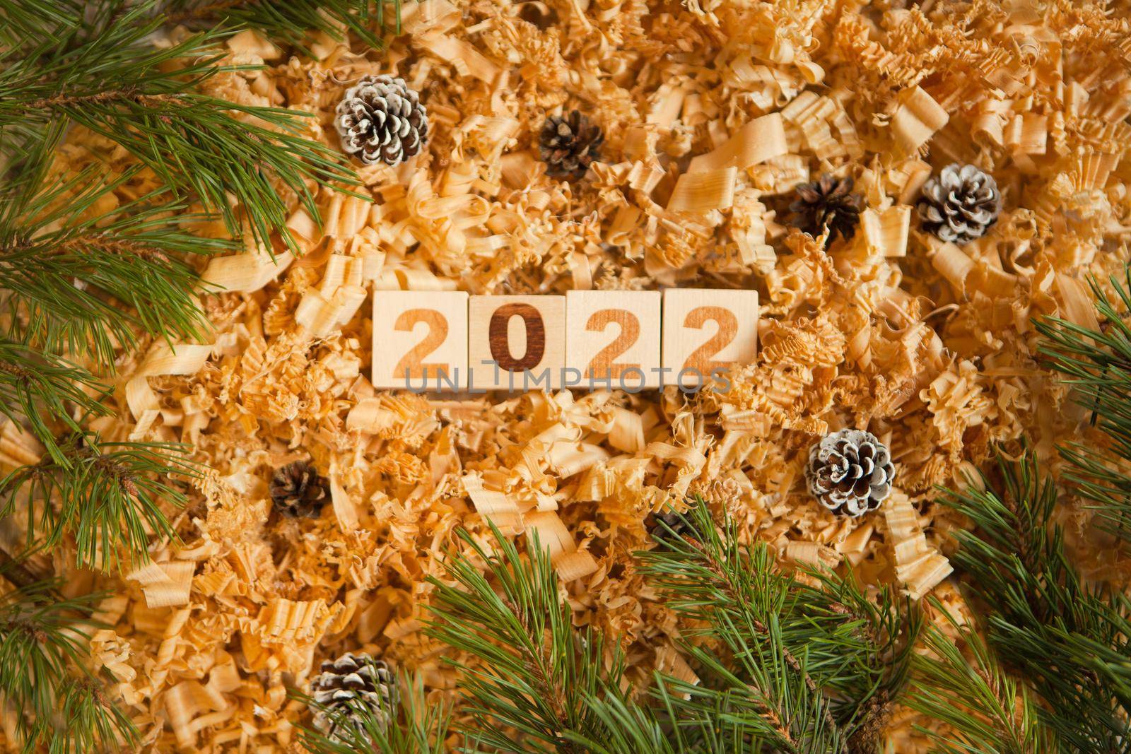 wooden numbers 2022 cubes symbolizng new year celebration. pine cones and shavings near pine-tree. brown warm colors