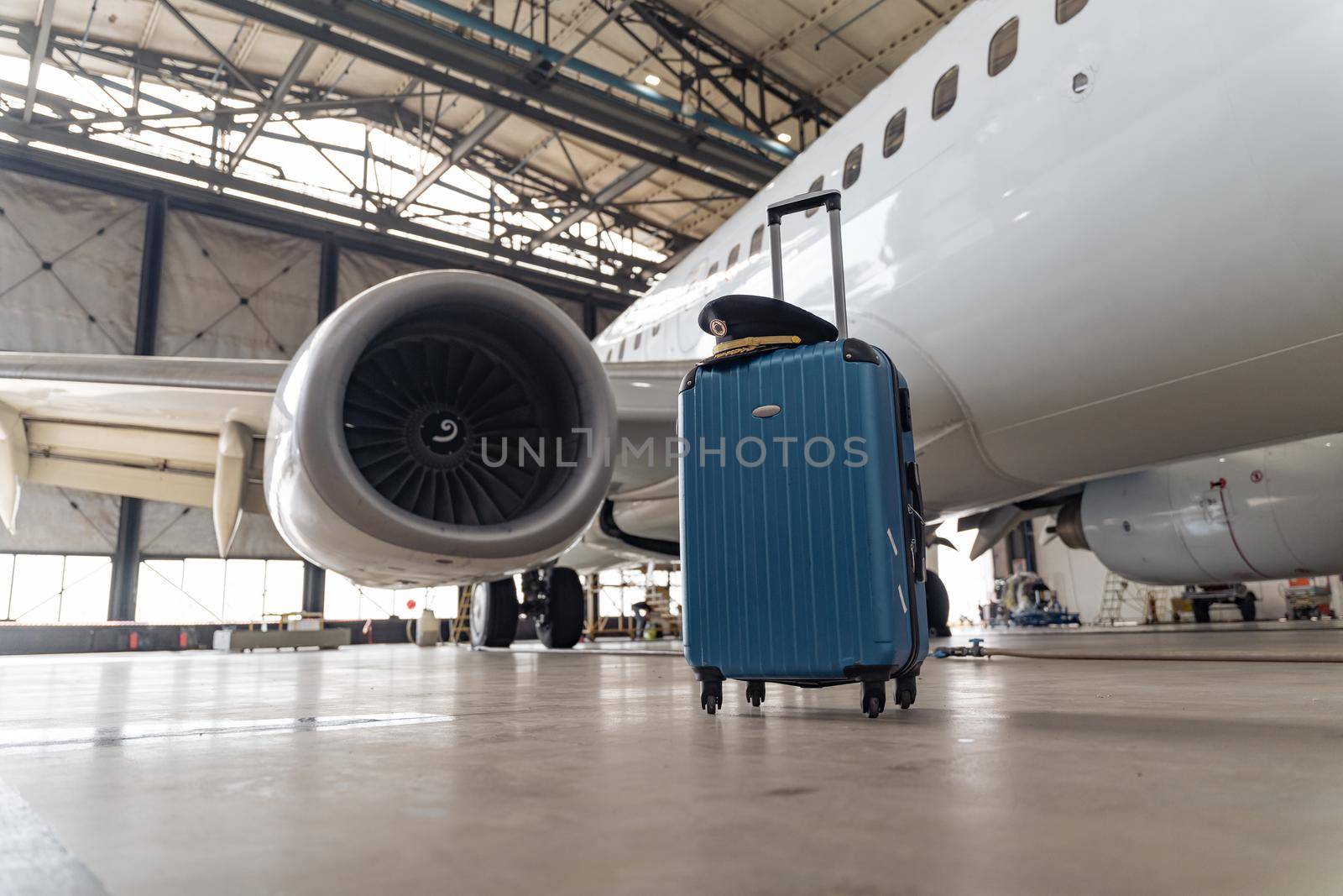 Blue suitcase in a hangar with a pilot's cap on it against the backdrop of a white plane
