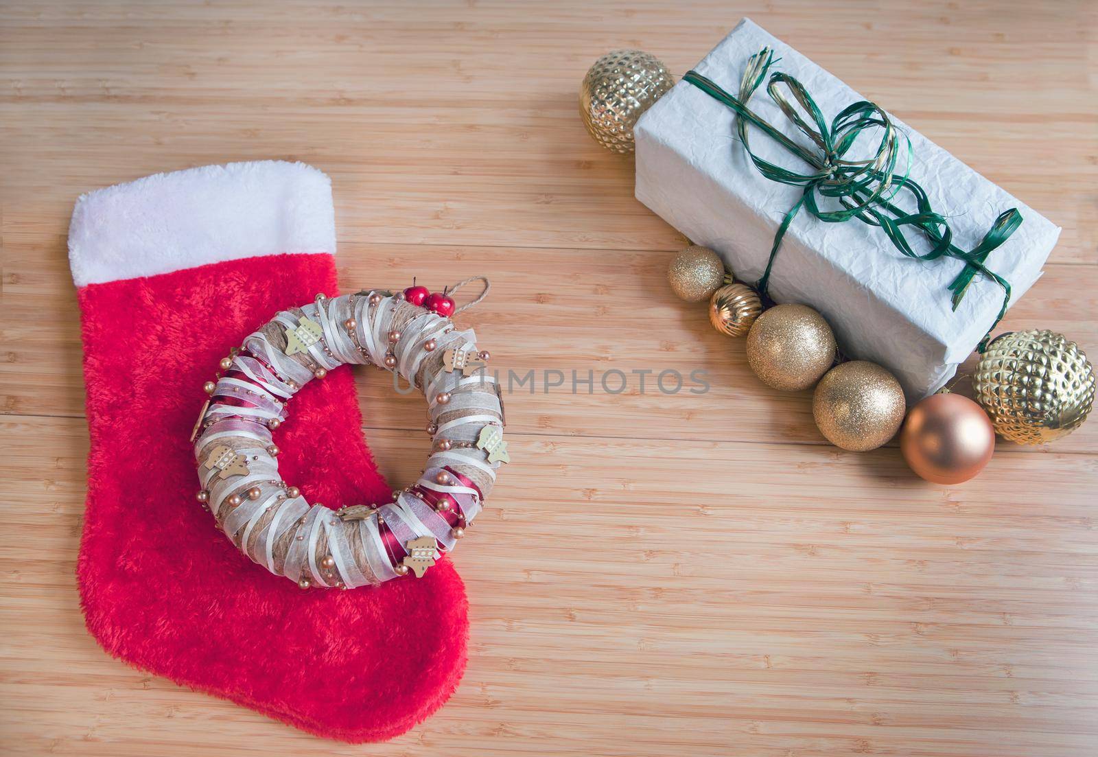 Red sock for Christmas gifts, present packed on recycled paper, golden balls decorations on wooden table. Beautiful Christmas card.