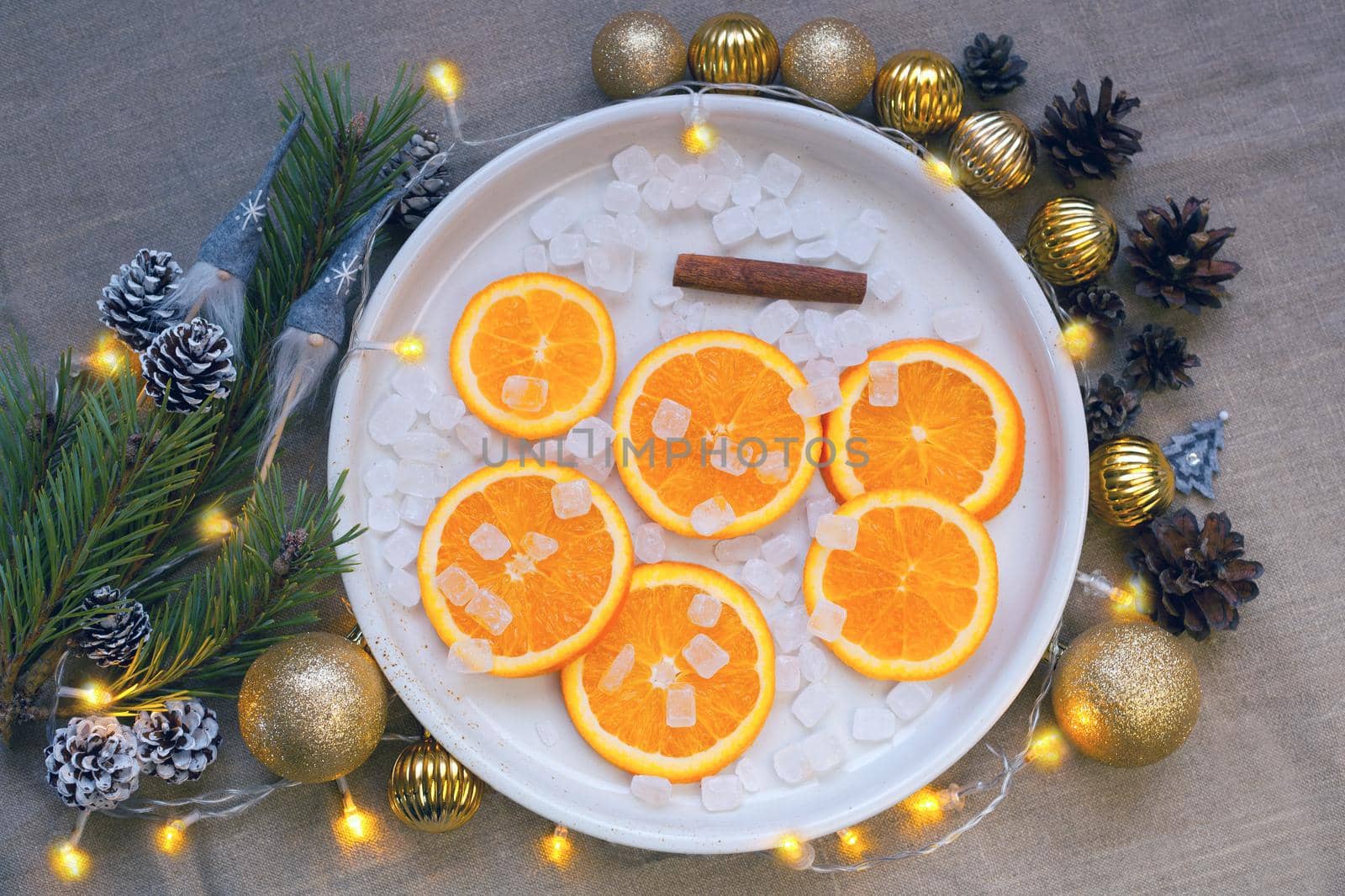 oranges at the plate near christmas tree branch, candies, cinnamon, golden balls and pine cones. Cristmas decorations. Tangerines and on plate