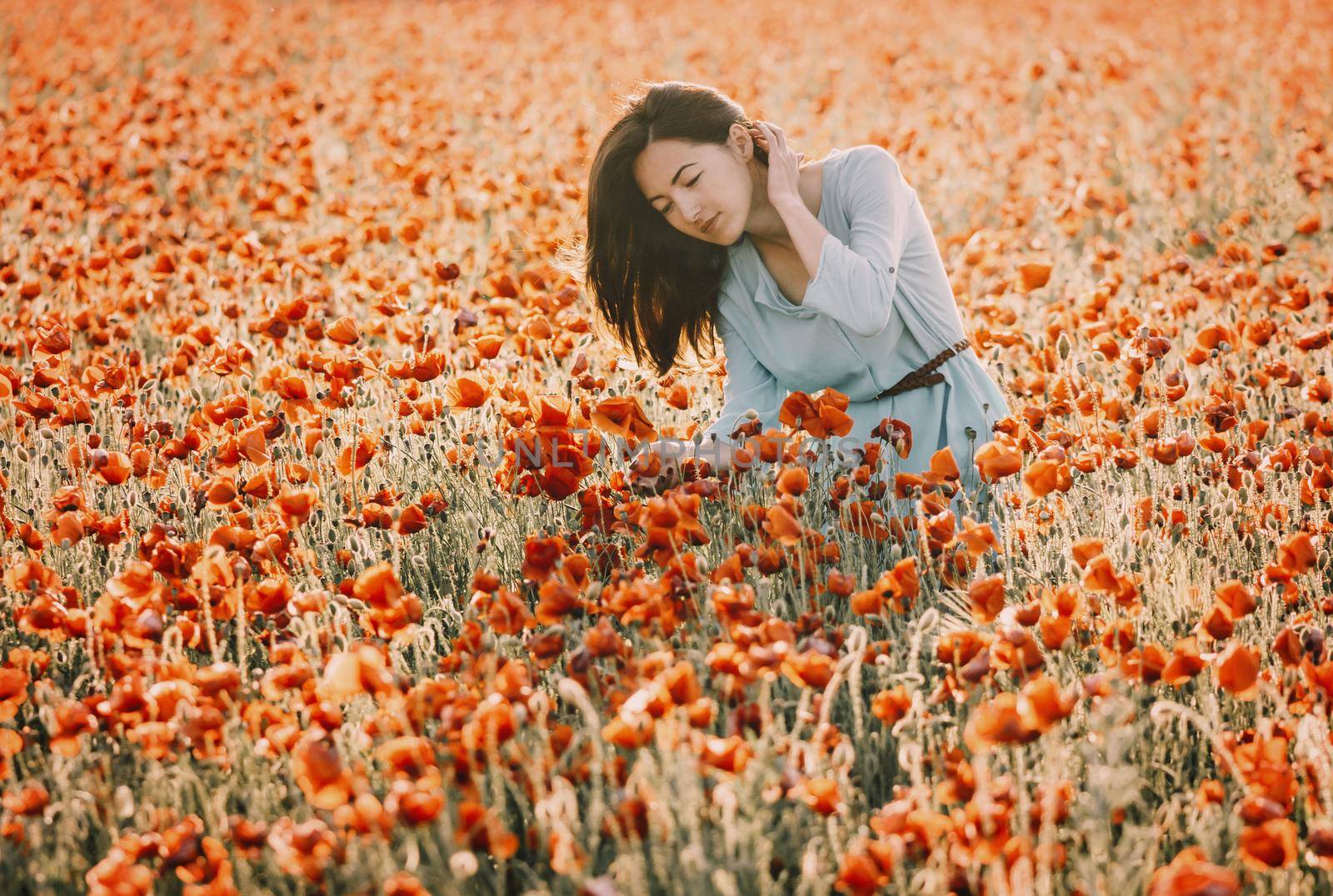 Romantic beautiful young woman walking in summer poppy flower field.