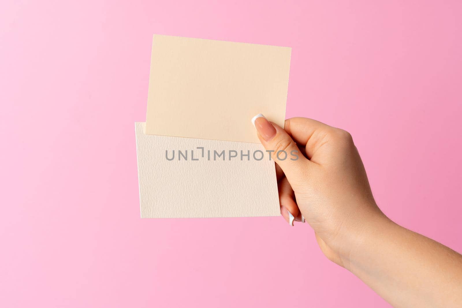 Woman hand showing blank business card on pink background. Close up.