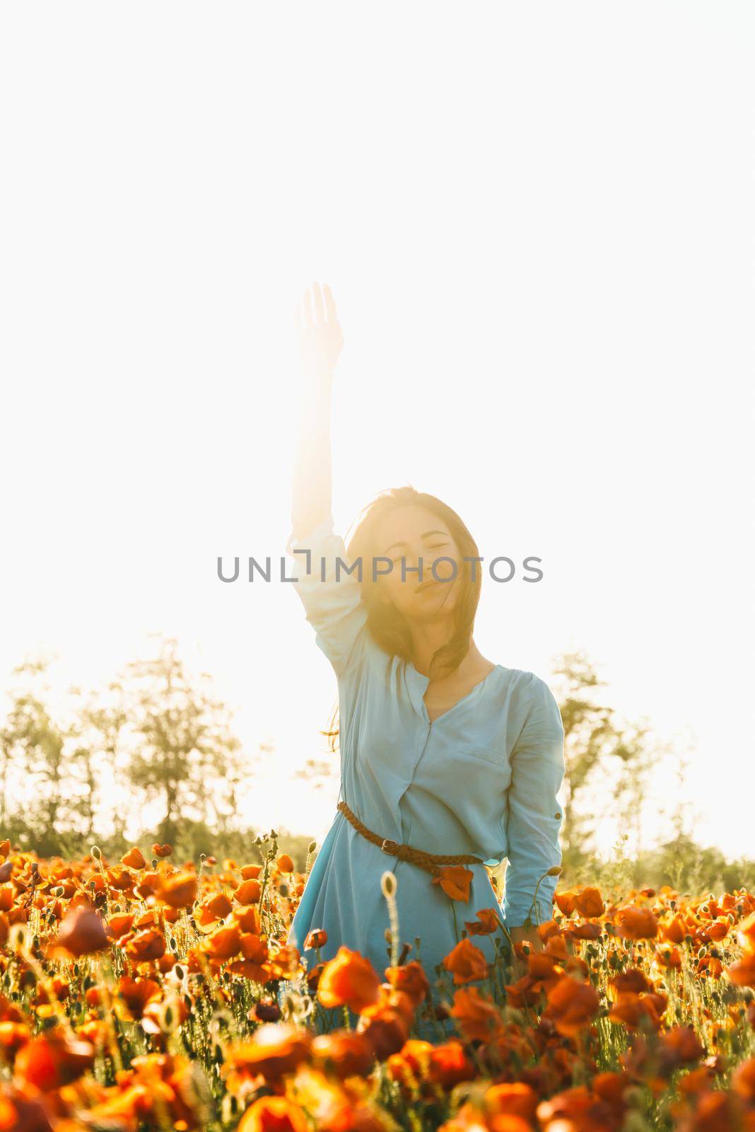 Dreaming beautiful young woman enjoying of sunny day in poppy flower meadow, summer vacations.