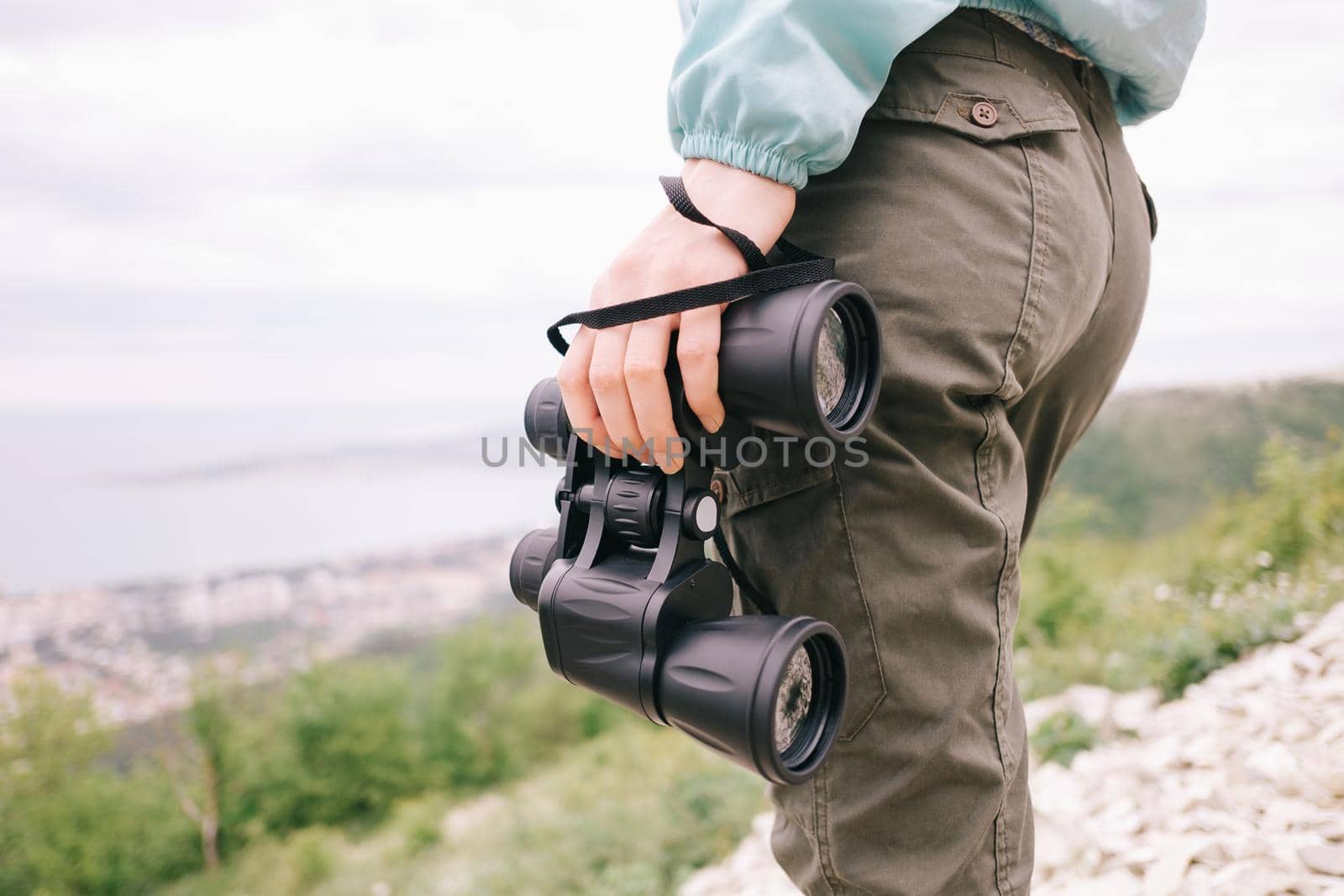 Unrecognizable hiker woman standing with binoculars in summer mountains, view of legs.