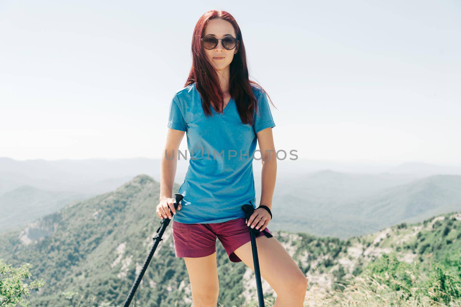 Beautiful sporty young woman in a t-shirt and shorts walking with trekking poles high in summer mountains.
