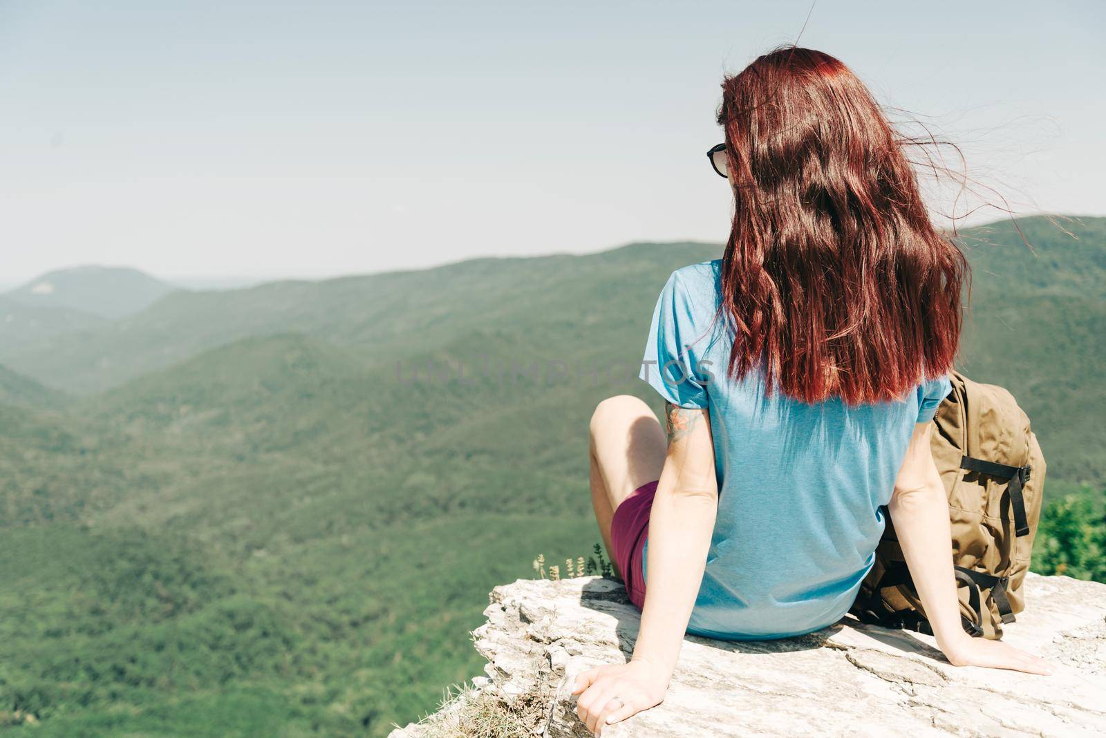 Explorer hiker young woman with backpack resting on top of rock high in summer mountains outdoor.