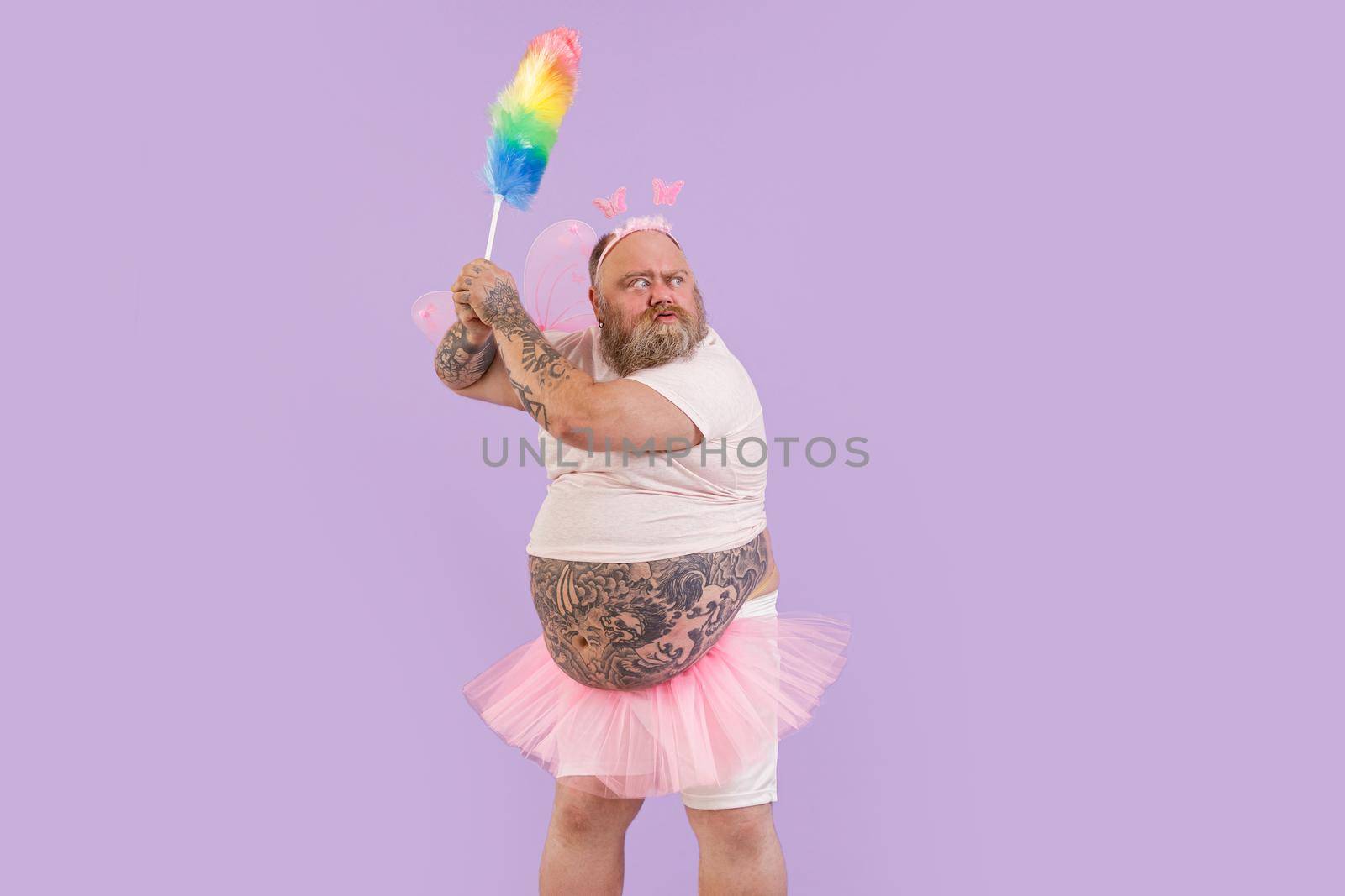 Bellicose actor man with overweight in fairy suit holds dust brush on purple background by Yaroslav_astakhov