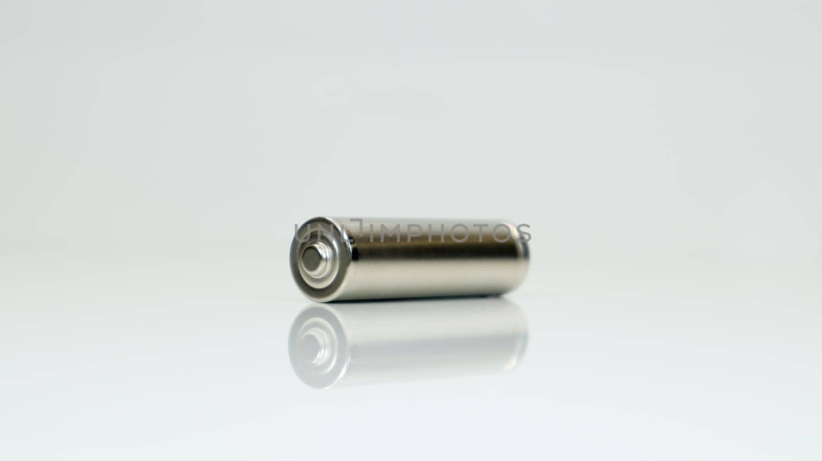 AA alkaline rechargeable battery on white glossy background with reflection. Close one empty battery with copy space