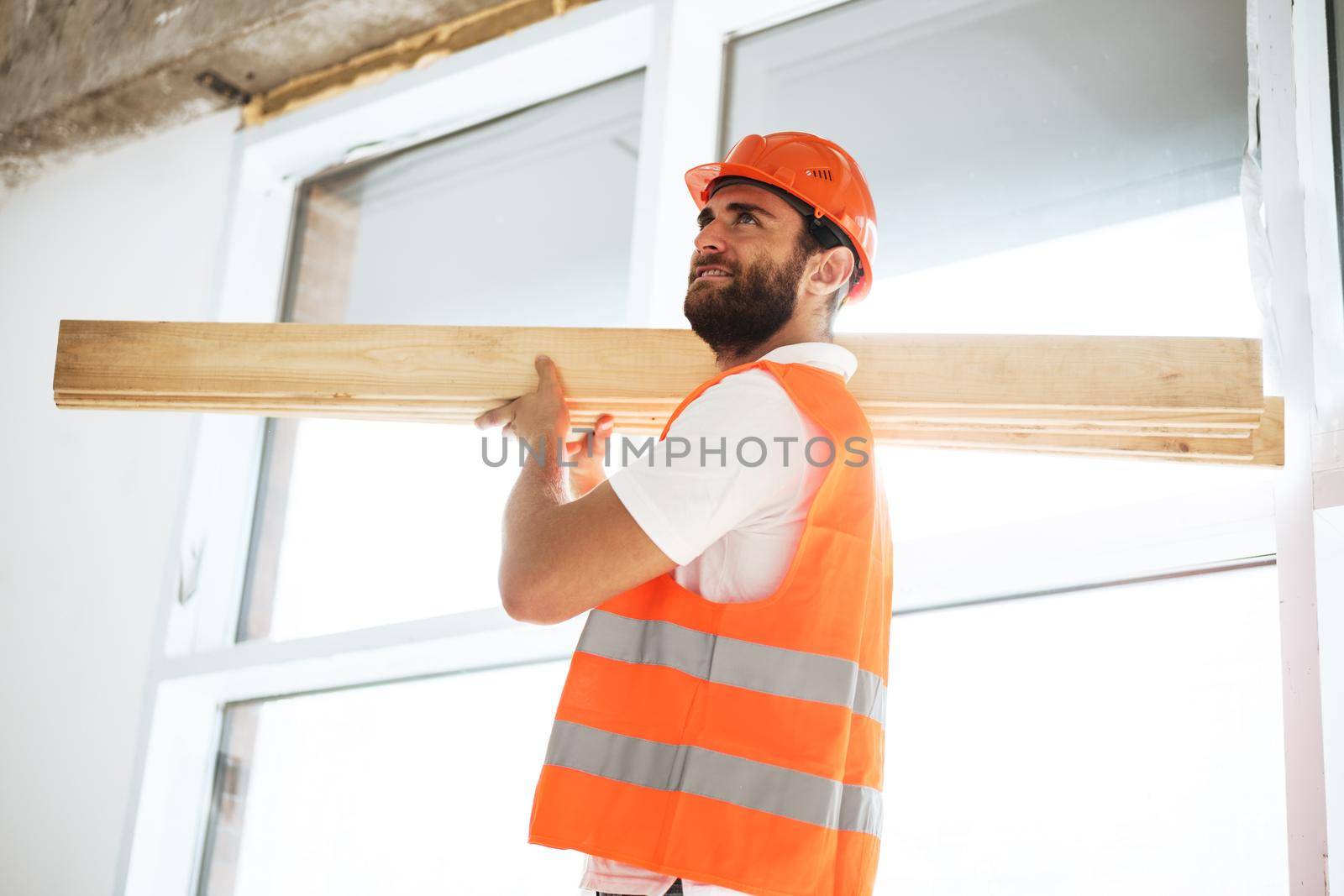 Builder man in hardhat carrying timber on building site, close up portrait