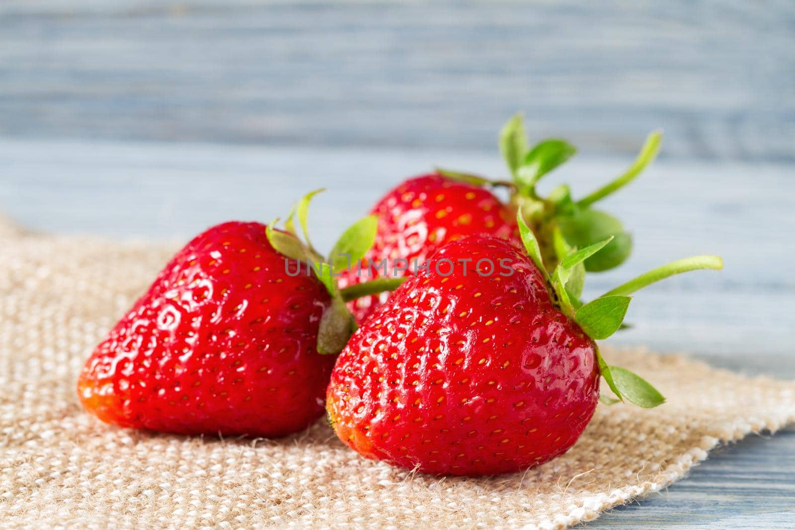 Fresh ripe strawberries on burlap on the blue wooden background. Selective focus.