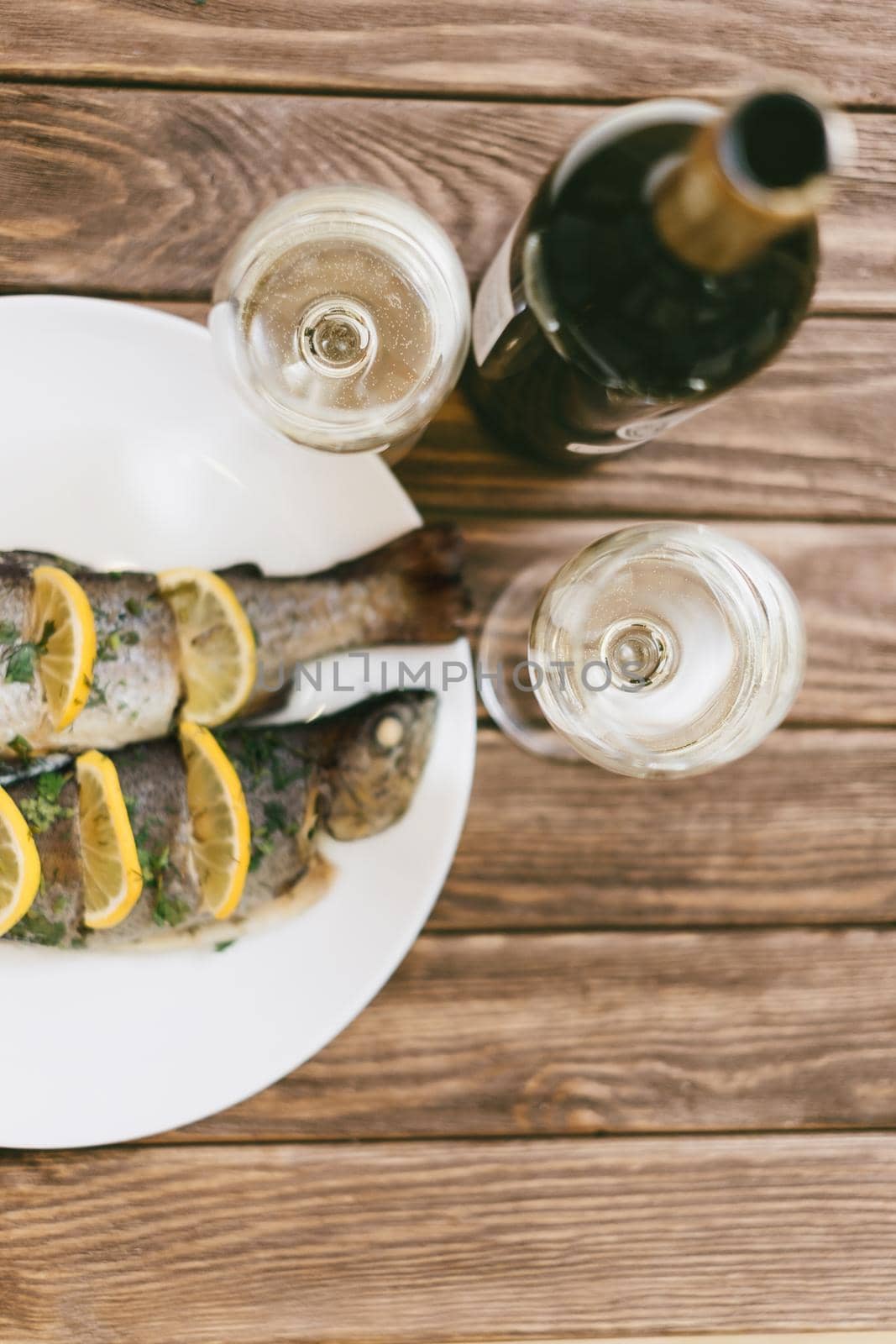 Baked fish dish and two glasses of white wine. by alexAleksei