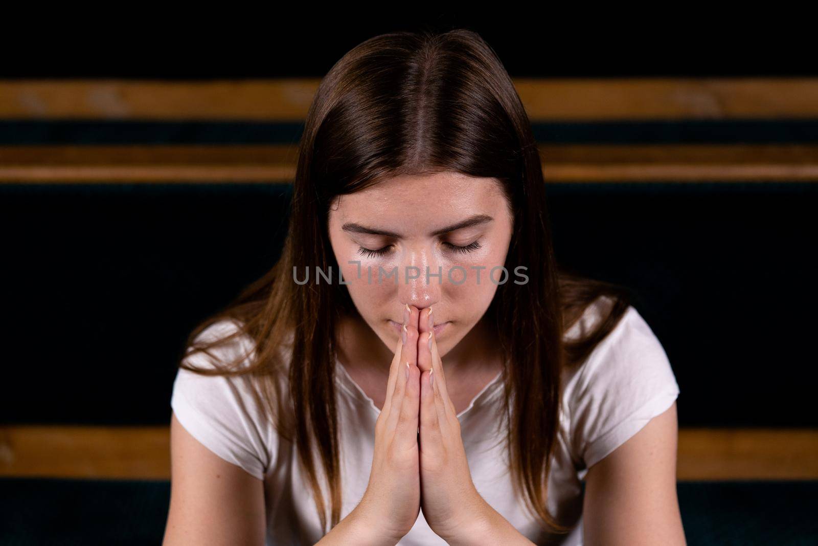 A Christian girl in white shirt is sitting and praying with humble heart in the church.