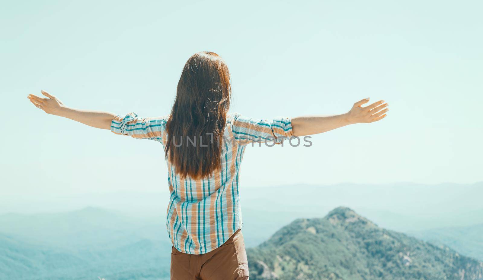 Freedom explorer young woman standing with raised arms high in summer mountains outdoor, rear view.