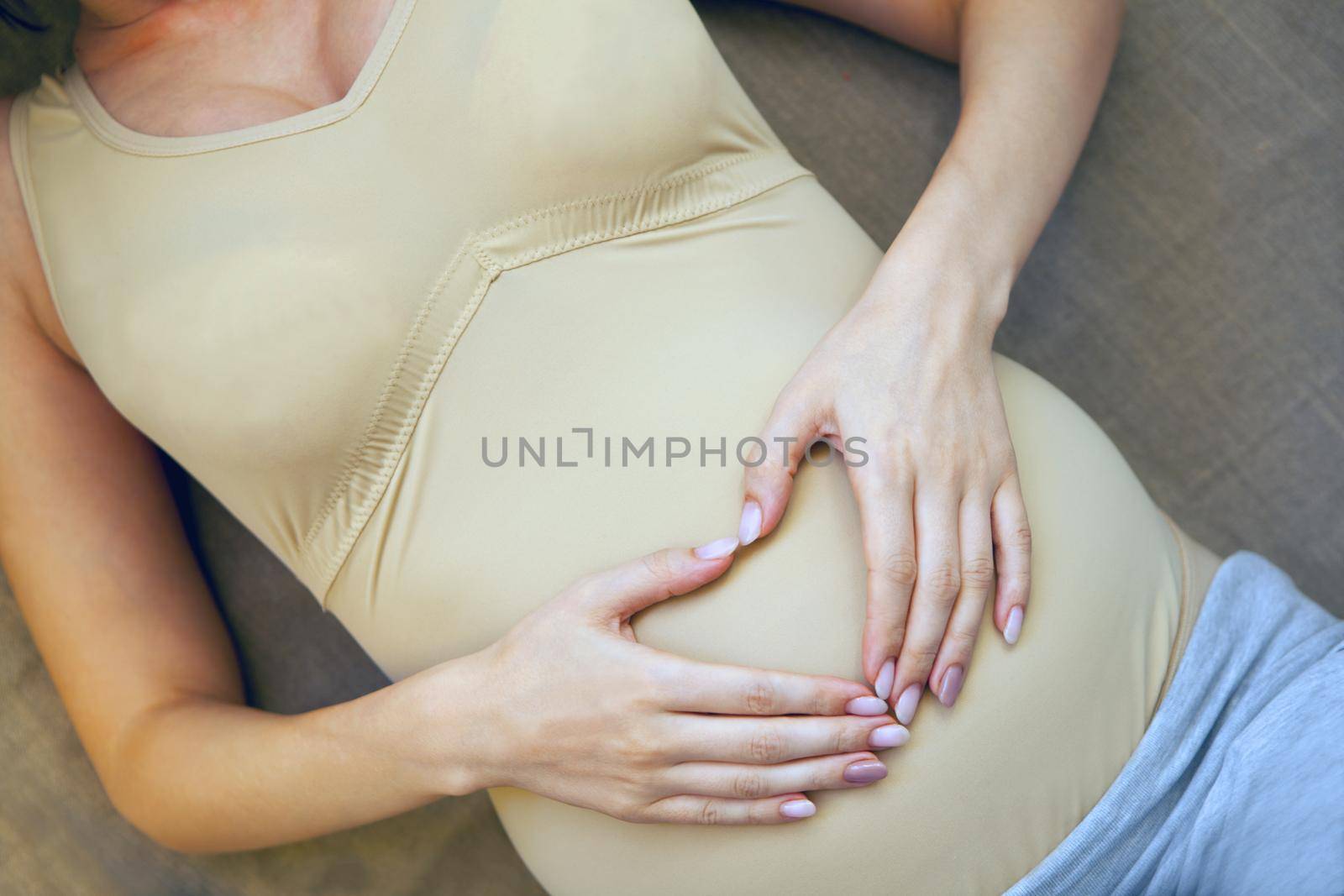 pregnant belly. woman hands in heart shape. Pregnant woman holding heart shaped hands on her belly. Mothernity brown colors