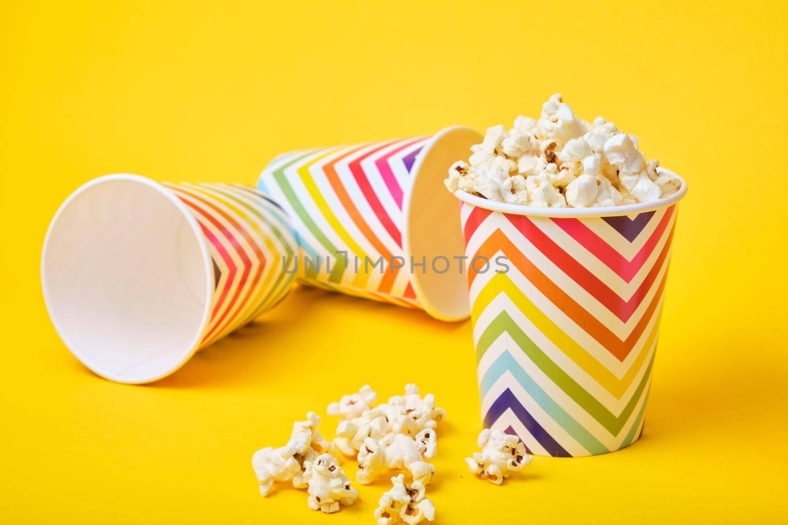 popcorn in a bright festive paper cup on a yellow background, tumbled glasses on a background by natashko