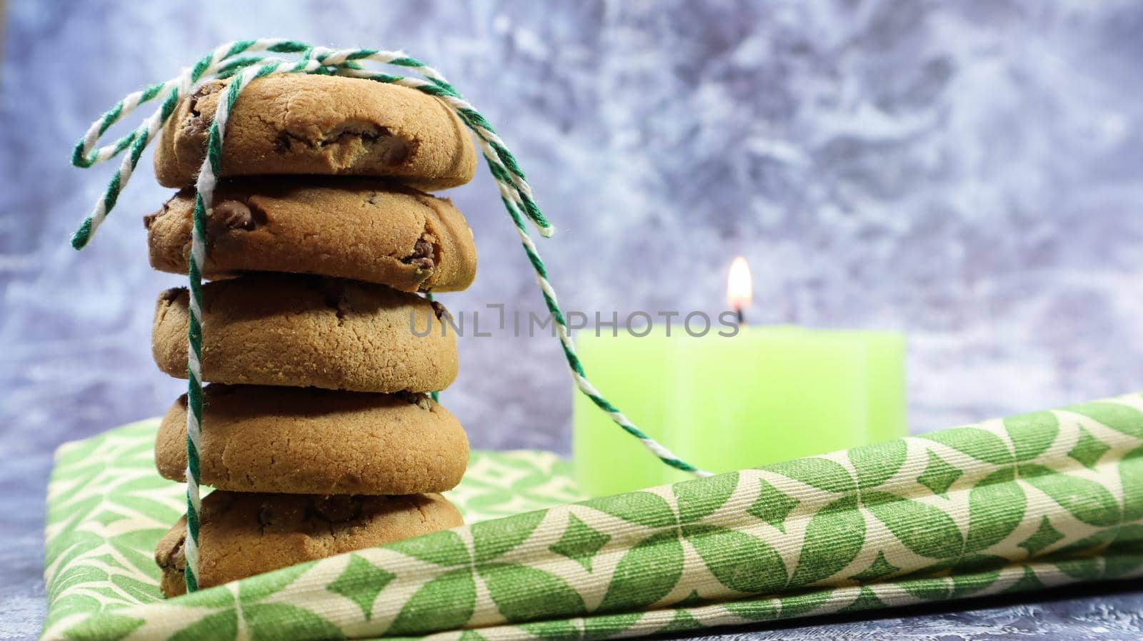 American chocolate chip cookies in a stack tied with thread on a green napkin and a candle. Traditional rounded crunchy dough with chocolate chips. Bakery. Delicious dessert, pastries