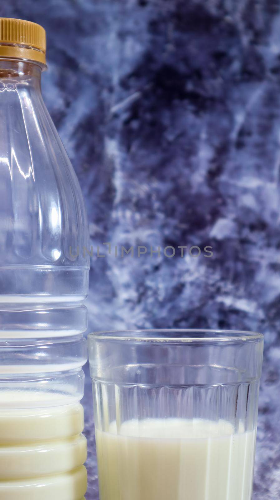 A plastic bottle of fresh regular milk and a glass beaker on a dark gray marbled or concrete background. Close-up front view. World milk day concept. Vertical photography. by Roshchyn