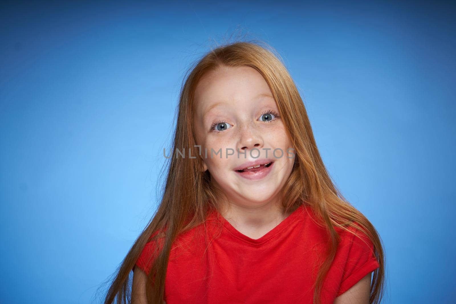 cute red-haired girl in red t-shirt emotions blue background. High quality photo