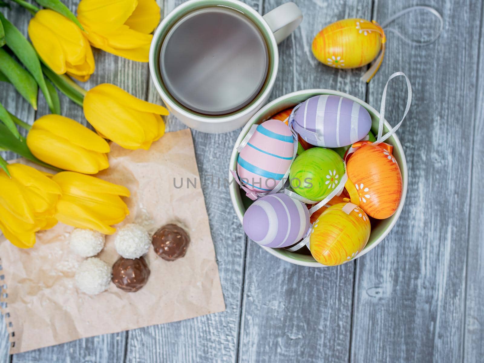 Easter eggs and tulips are on the table. View from above. Tea in a white cup and chocolates by Utlanov