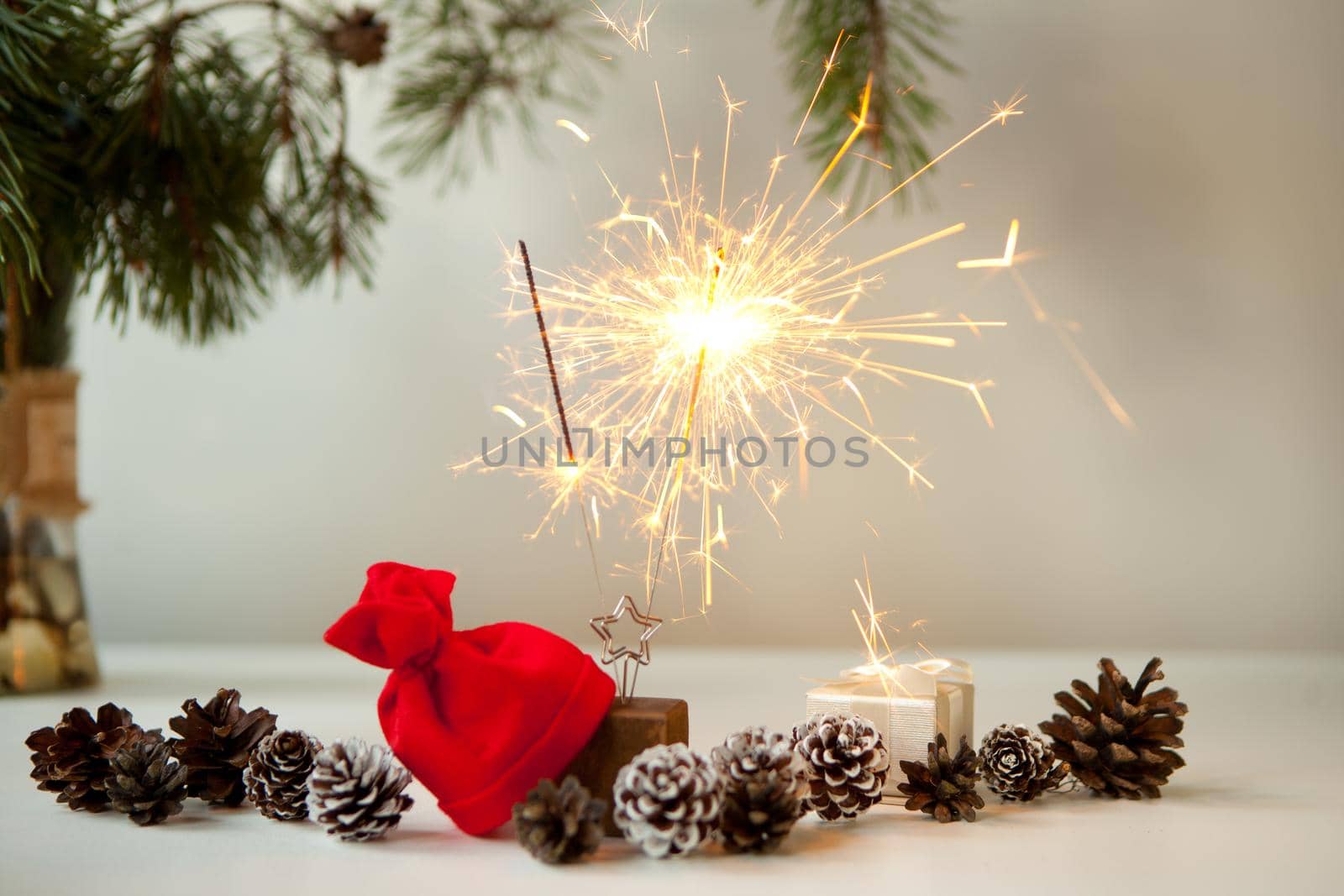 festive sparkles near pine cones, christmas tree branch with golden bokehand red christmas hat. New year party burning sparkler closeup on white background. fireworks, shining fire flame. Christmas light