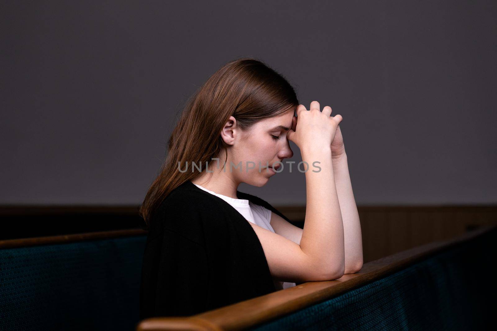 A Christian girl in white shirt is sitting and praying with humble heart in the church.